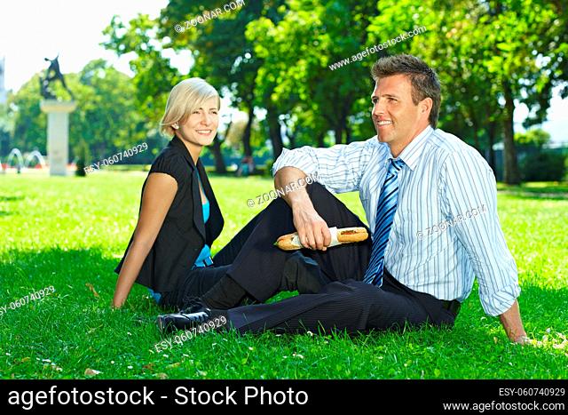 Young businesspeople sitting on grass and having lunch outdoor in city park summertime