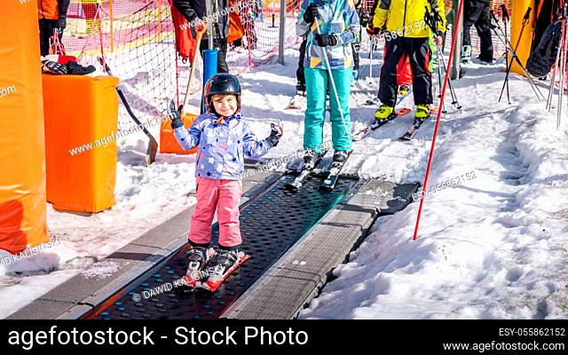 Young, happy skier girl going up on conveyor lift belt to green ski zone for ski lessons, Bialka Tatrzanska, Tatry, Poland