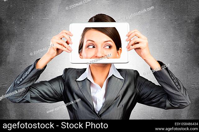 Portrait of woman covering her face with tablet computer. Businesswoman showing tablet PC with woman face on screen. Corporate businessperson on grey wall...