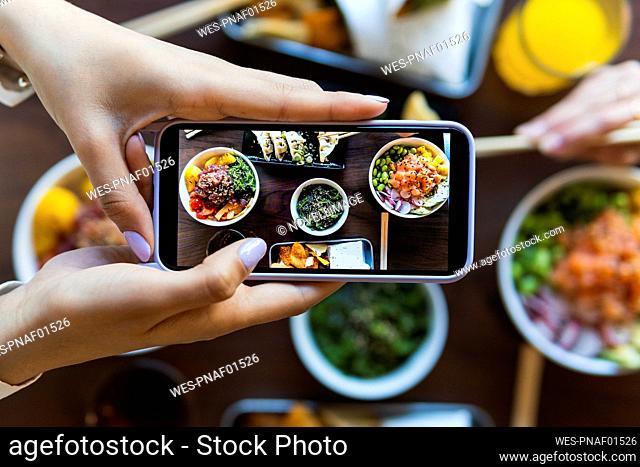 Young woman photographing food at table in restaurant