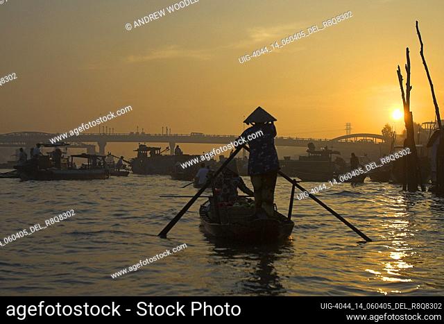 Woman in conical hat rows river boat with fruit at sunrise Cai Ran floating market near Can Tho Vietnam