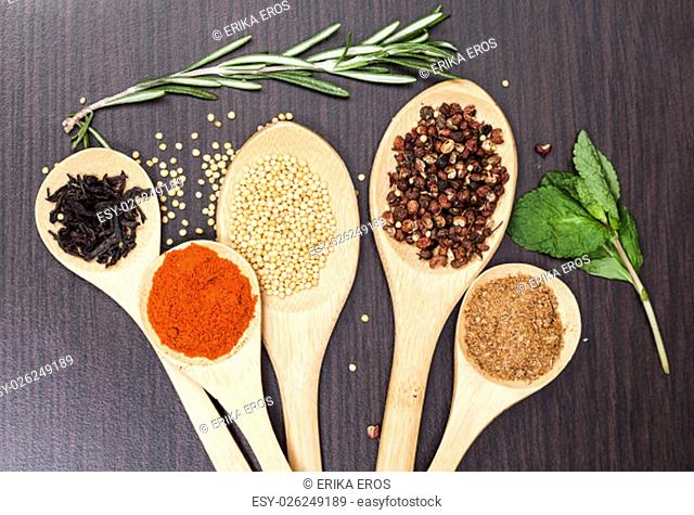 Various colorful spices and wooden kitchen spoons on black background