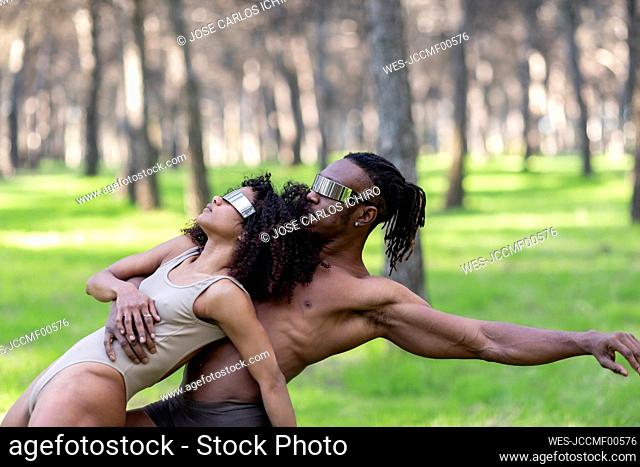Two professional dancers wearing futuristic goggles performing in middle of forest