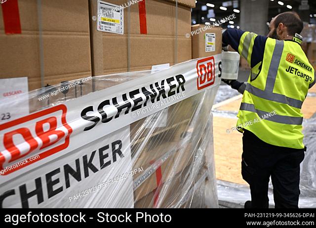 PRODUCTION - 07 December 2023, Hesse, Frankfurt/Main: A DB Schenker Jetcargo employee applies adhesive tape to a pallet of freight in the logistics company's...