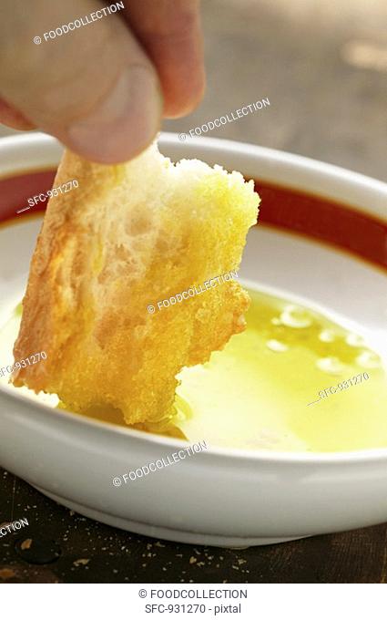 Hand dipping a piece of white bread into a bowl of olive oil