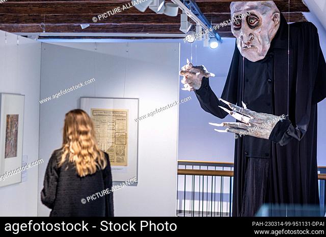 14 March 2023, Mecklenburg-Western Pomerania, Wismar: A woman stands next to the theater figure Nosferatu in the special exhibition ""Golden 20s - Gray 20s...