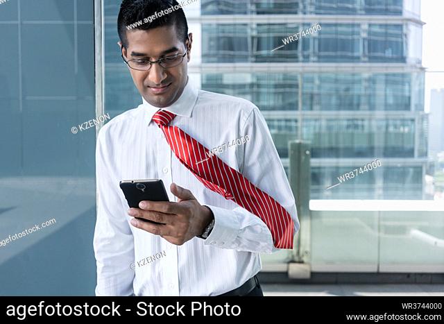 Portrait of an Indian businessman smiling while reading information on the mobile phone indoors