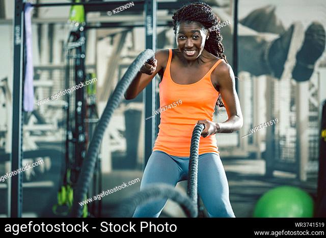 Low-angle view of a strong and beautiful African American woman exercising alternative waves with battle ropes, during functional training workout at the gym