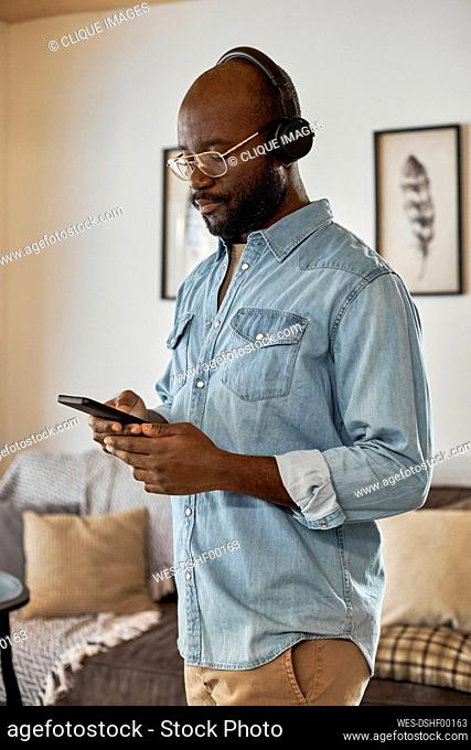 Young man with headphones using smart phone standing at home