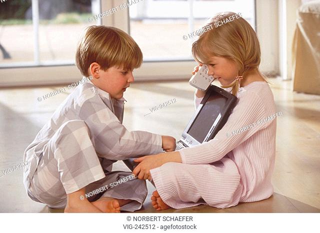 indoor, blond girl and boy, 5- 6 years old, wearing night-dress and pyjama sit on the wooden floor playing with the laptop  - GERMANY, 26/02/2005