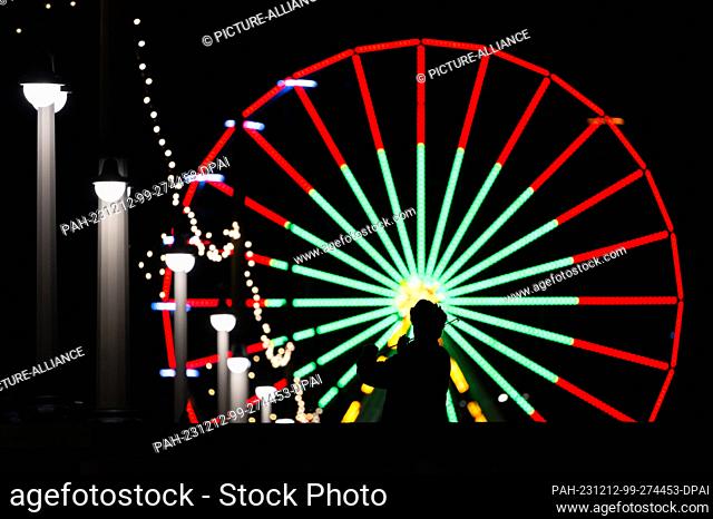 12 December 2023, Saxony, Dresden: A street musician plays the violin on the Augustus Bridge, a Ferris wheel from the ""Augustusmarkt"" Christmas market on the...