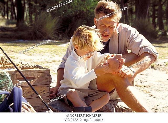 outdoor, blond 6-year-old boy helps his father in a forest to remove a thorn out of his foot  - GERMANY, 19/09/2004