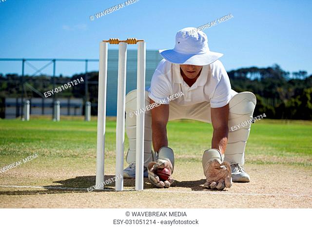 Wicketkeeper holding ball behind stumps against blue sky