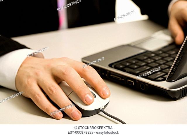 Human hands touching computer mouse and keys of opened laptop