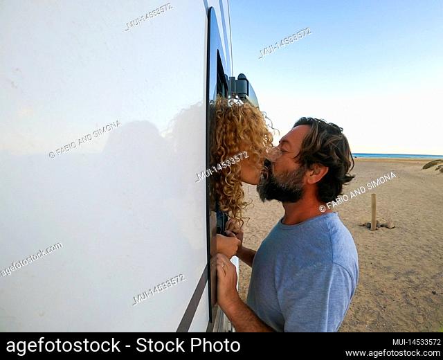Adult man and woman kissing during summer holiday vacation. Mature man outside a camper van kiss her wife inside it. Travel destination at the beach