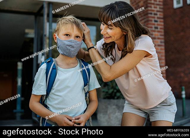 Mother helping son to wear protective face mask while going to school
