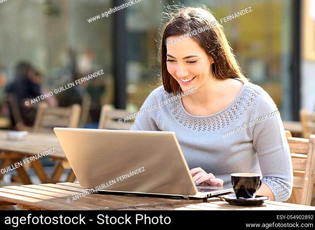Happy young woman using laptop in a coffee shop terrace
