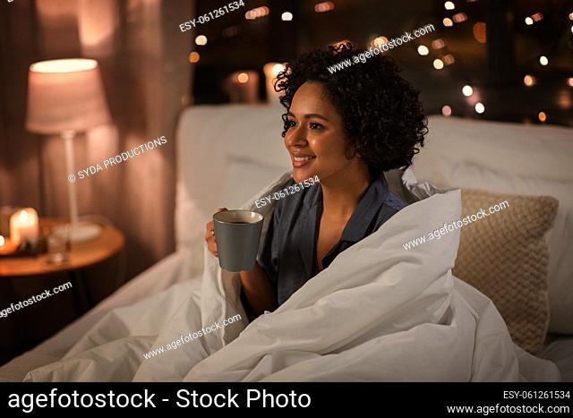 happy woman with coffee sitting in bed at night