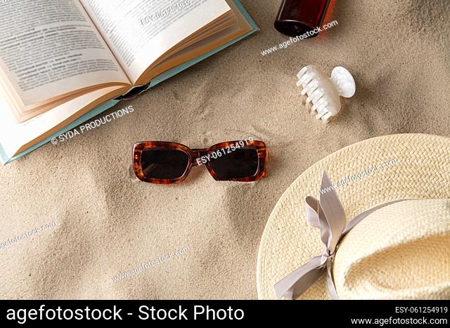 book, sunglasses and sunscreen on beach sand