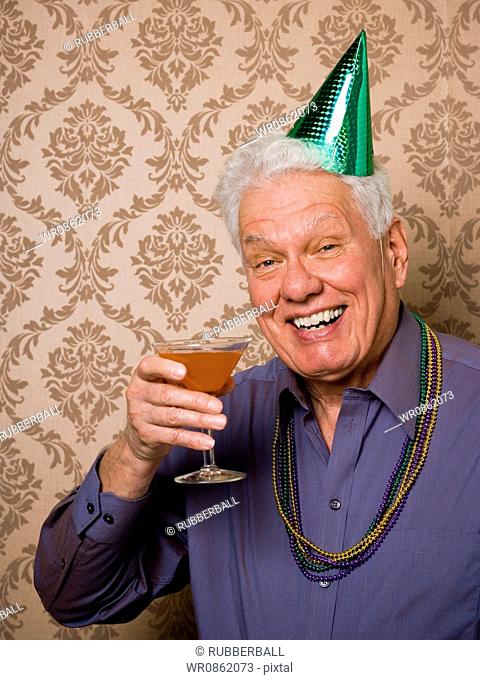 Portrait of a senior man holding a glass of martini and wearing a party hat