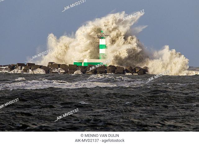 Big waves crashing against the lighthouse at the tip of the pier of Ijmuiden, Netherlands, during severe storm over the North Sea