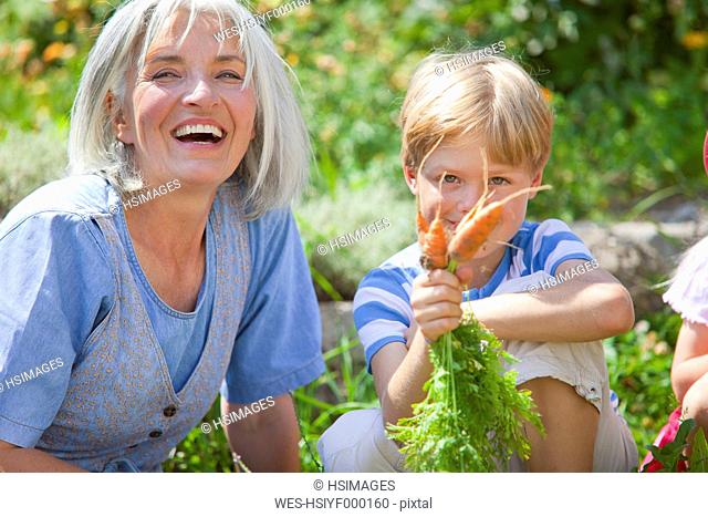 Germany, Bavaria, Mature woman and boy inspecting carrots in garden