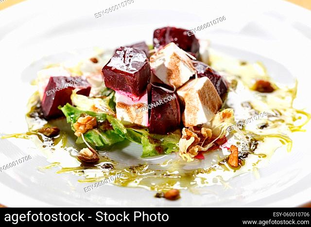 Healthy Beet Salad with fresh sweet baby spinach, kale lettuce, nuts, feta cheese. on a white plate, the dish is served in the restaurant