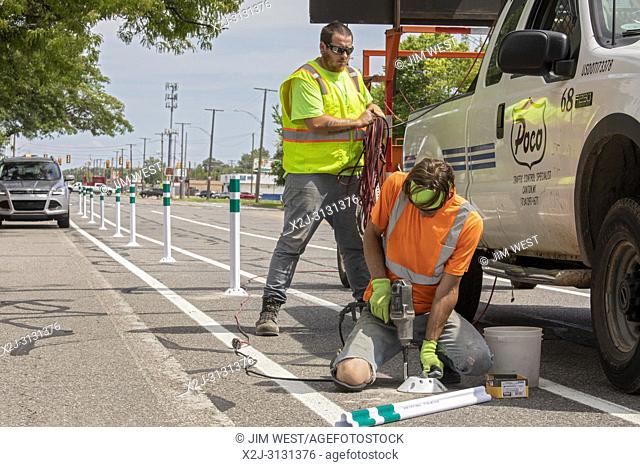 Detroit, Michigan - Workers install bollards as they construct bicycle lanes on a busy street. The city is dramatically expanding protected bike lanes
