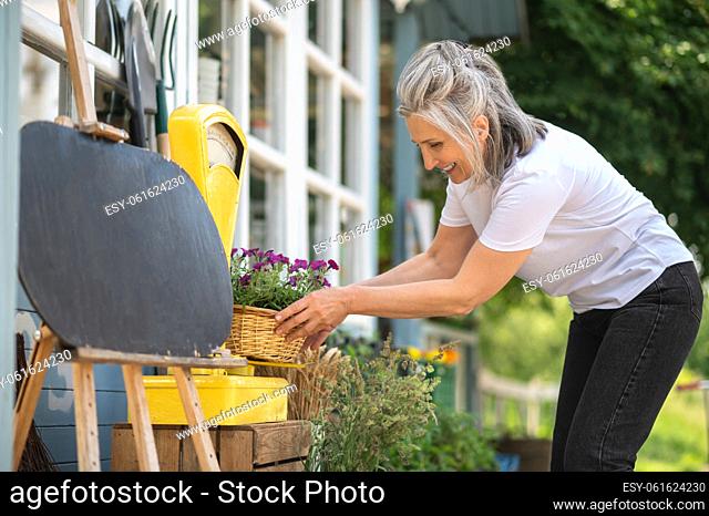 Gardening. A woman in white thsirt spending time in the graden and looking busy