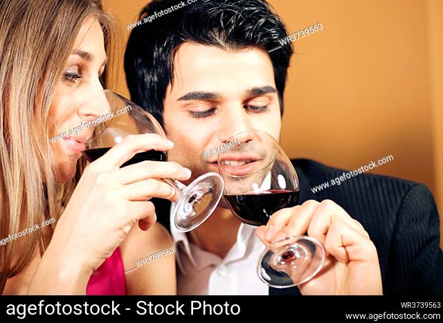 Young couple - man and woman - in a restaurant drinking glasses of red wine; focus on the face of woman