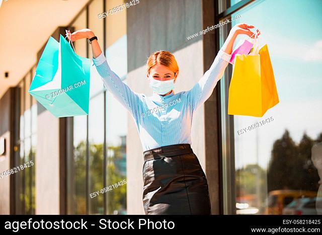 Young attractive girl walking full of positive emotions after first shopping after long break due to pandemic. New realia of life and shopping in protective...