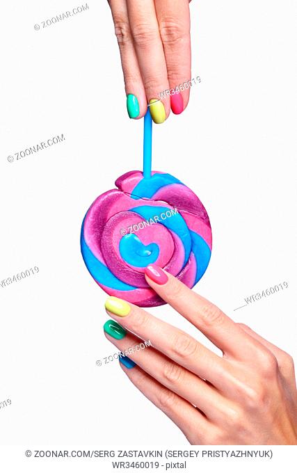 Woman is holding lollipop candy. Female fingers with bright green, yellow, pink and blue nails manicure. Girl's hands isolated on white background