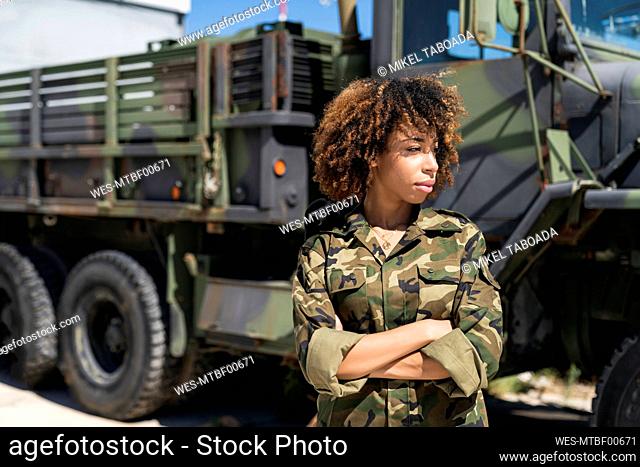 Young female army soldier with arms crossed looking away while standing against truck at military base