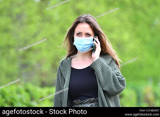 Topic image Corona: A young woman with protective mask, face mask, community mask is on the phone on April 24th, 2020. | usage worldwide
