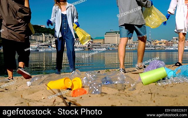 Group of activists friends collecting plastic waste on the beach. People cleaning the beach up, with bags