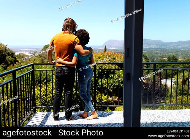 Happy diverse couple standing on balcony embracing