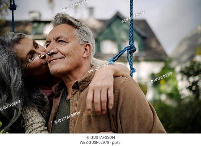 Happy woman hugging an kissing senior man on a swing in garden