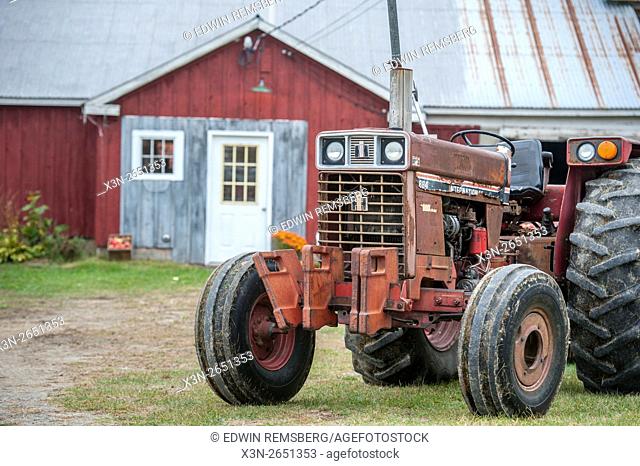 Old red tractor in front of a barn on an orchard in Livermore, Maine
