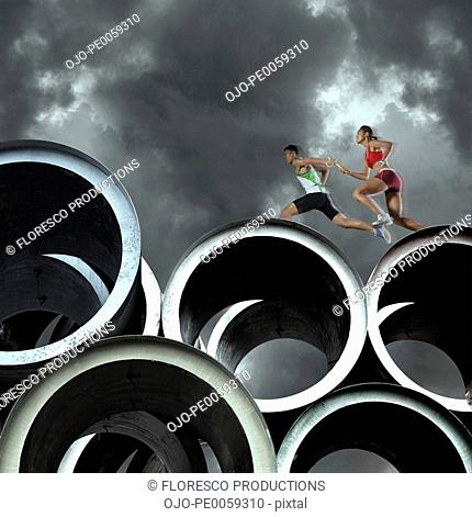 Two relay runners going across large cylinders