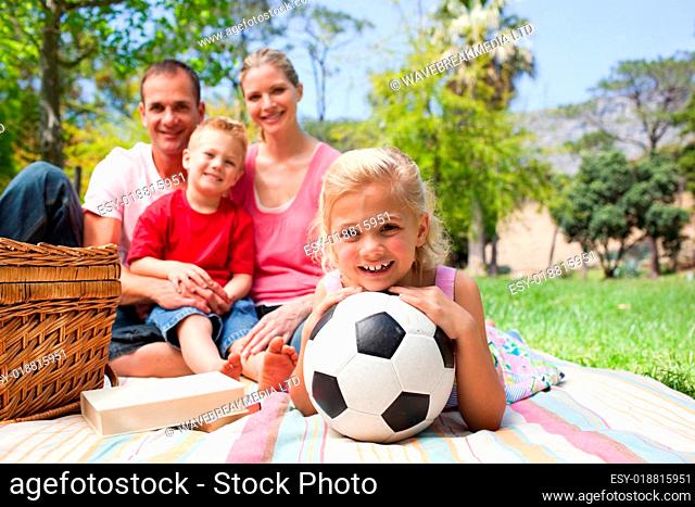 Little blond girl holding a soccer ball at a picnic