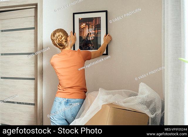 Woman mounting picture frame on wall in new apartment