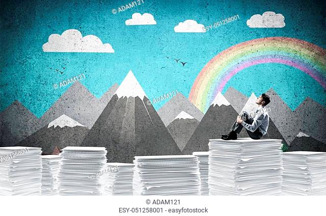 Thoughtful businessman looking away while sitting on pile of documents with drawn landscape on background. Mixed media