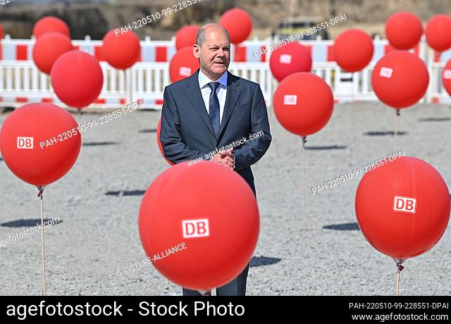 10 May 2022, Brandenburg, Cottbus: German Chancellor Olaf Scholz (SPD) stands between red balloons with the Deutsche Bahn (DB) logo for the symbolic...