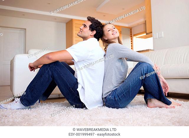 Side view of young couple sitting on the floor back-to-back