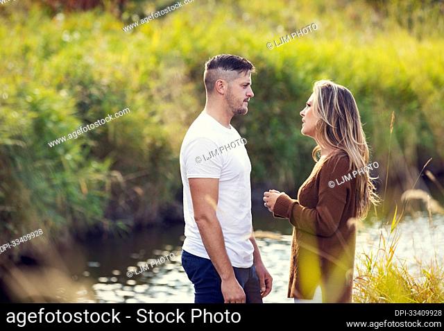 Husband and wife spending quality time together outdoors near a stream in a city park and having a serious discussion; Edmonton, Alberta, Canada
