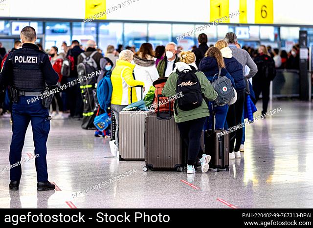 02 April 2022, Lower Saxony, Langenhagen: Numerous passengers wait next to a police officer in the early morning at Hannover-Langenhagen Airport