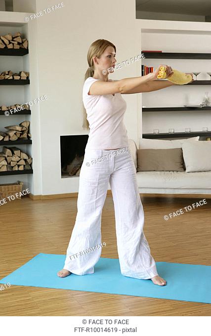 A blonde woman holds a towel as she stretches herself while exercising