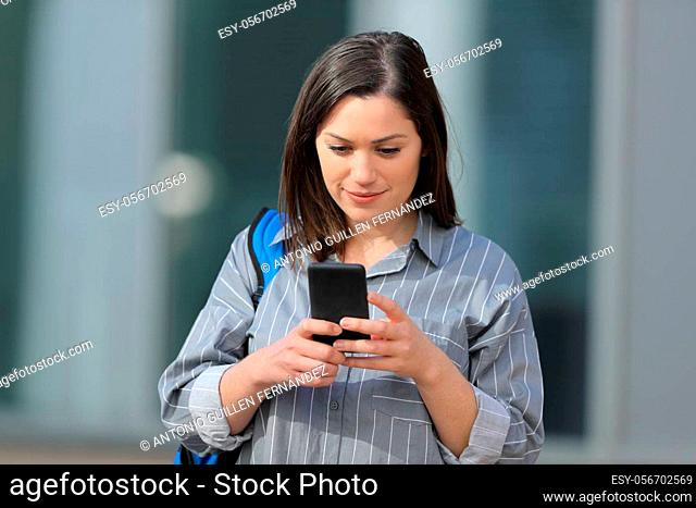 Front view portrait of a concentrated student checking smartphone walking in a campus