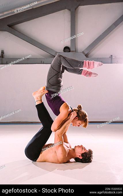 The theme of Acroyoga and Yoga Poses. Acroyogis practicing. with studio Backlight. the man Base holds in the Static poses a woman Flyer in the top above herself...