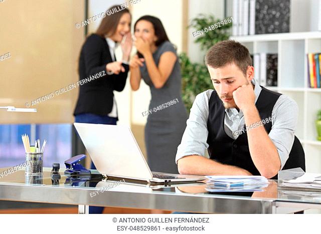 Two coworkers bullying a worried colleague that is sitting in his workplace at office